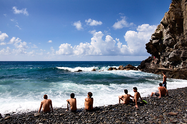 People Sitting on the Shingle at the Edge of the Waves