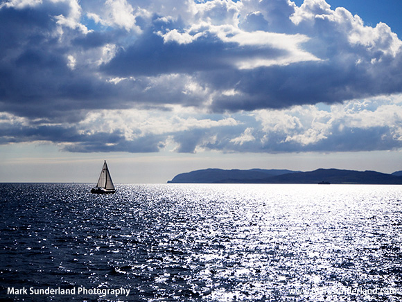 Yacht Sailing and Sunlight reflecting off the Sea in the Firth of Lorn with Mull beyond Argyll and Bute Scotland